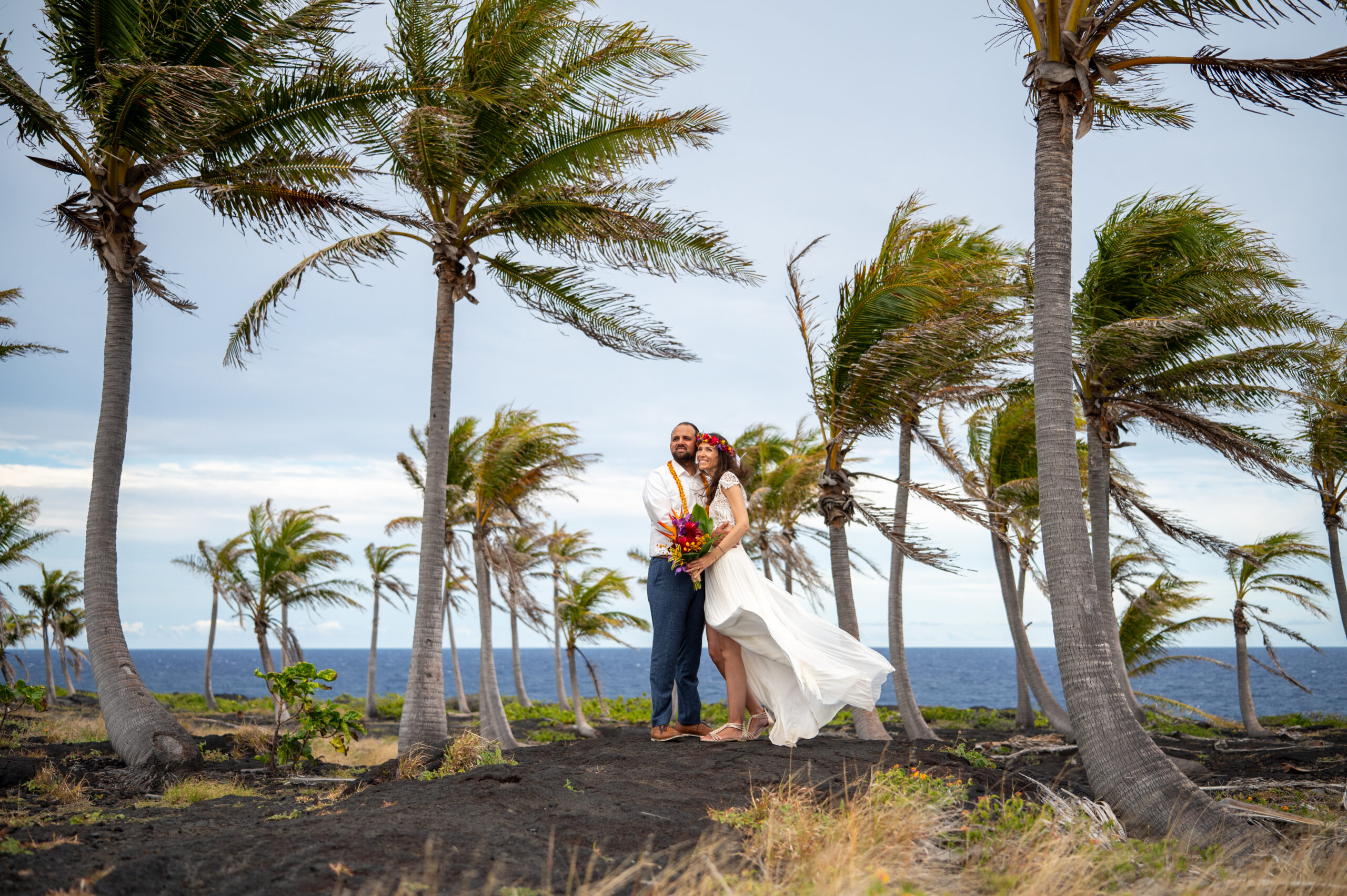 A bride and groom stand in a coconut palm grove in Volcanoes National Park