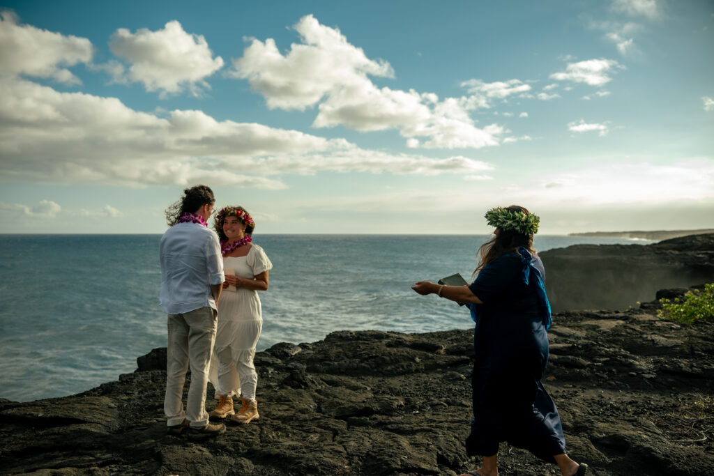 A couple and an officiant stand on the cliffside in Volcanoes National Park during their wedding ceremony