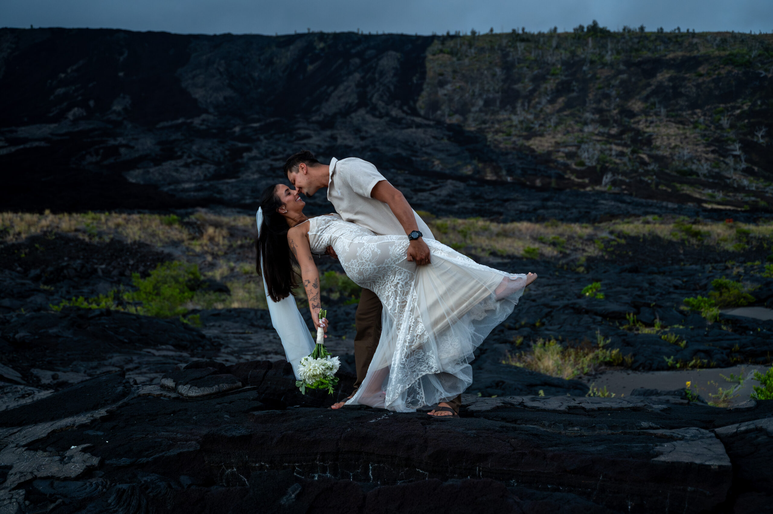 A couple on their wedding day kiss in front of a lava flow in Hawaii Volcanoes National Park