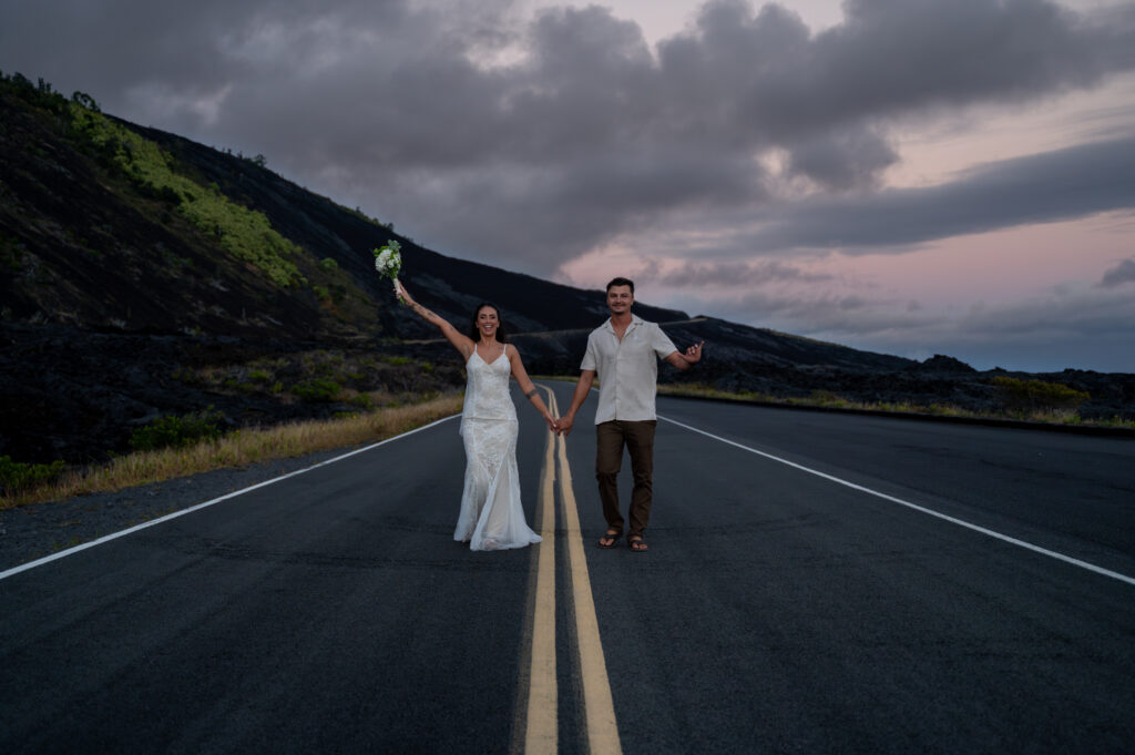 A couple in wedding clothes walks along the road in Volcanoes National Park