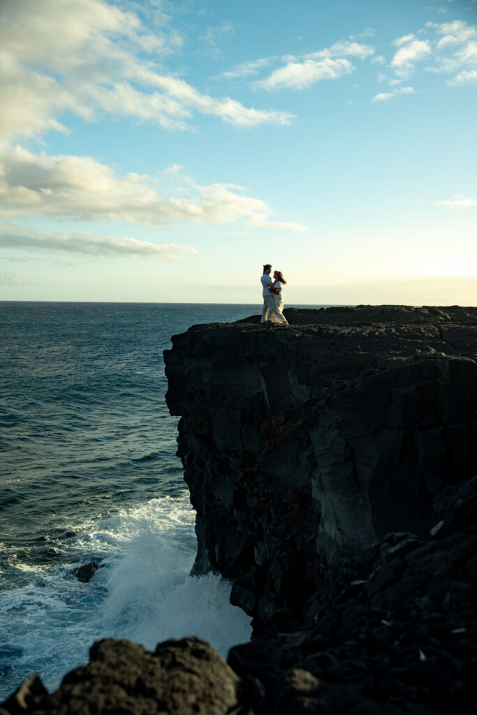 A couple stands on the edge of a cliff in Volcanoes national park