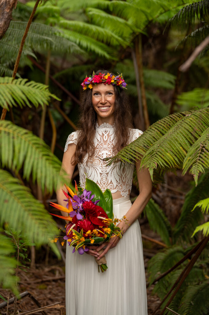 A bride stands framed by ferns and holding a tropical bridal bouquet
