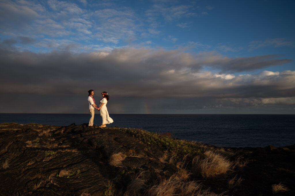 A couple stands on a lava rock formation in Hawai'i Volcanoes National Park overlooking the ocean