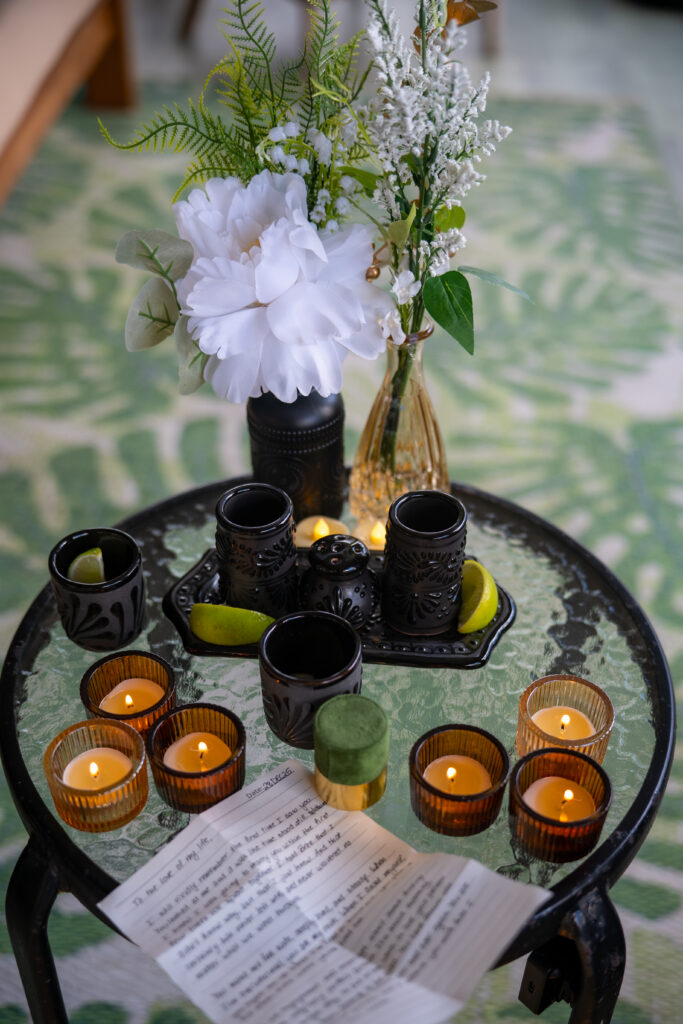 candles, shot glasses, flowers in a black vase and a hand written letter on a small glass table