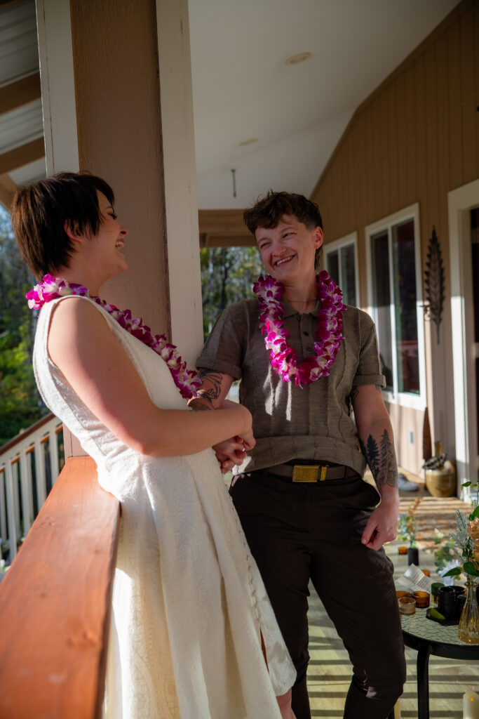 Two women wearing purple lei stand and laugh