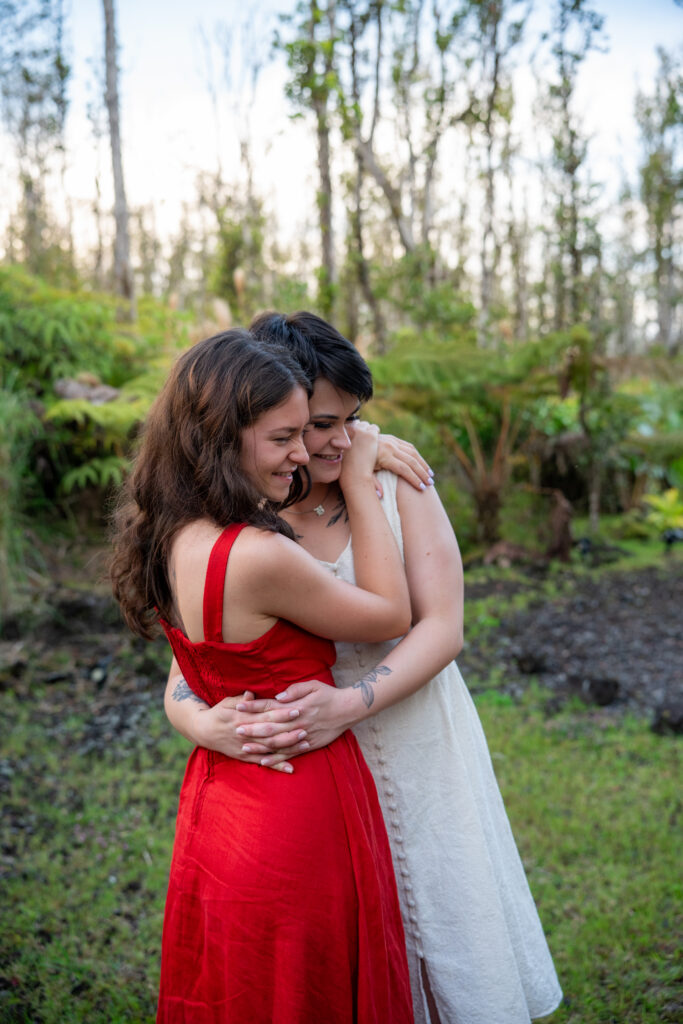 Two women embrace in front of a fern forest