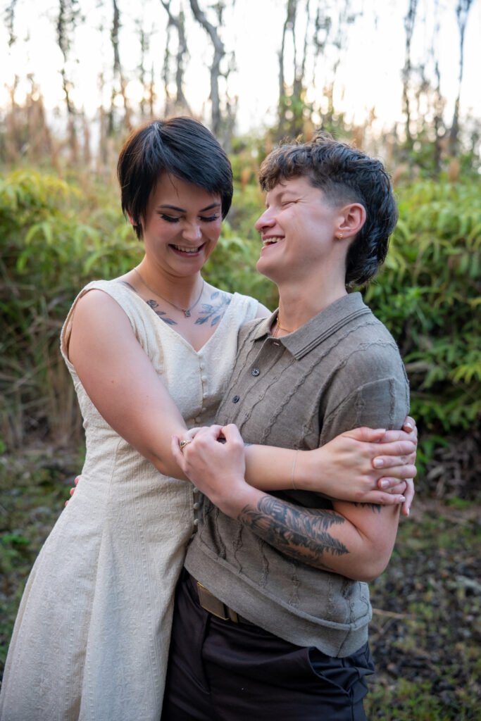A couple embraces in front of a fern forest
