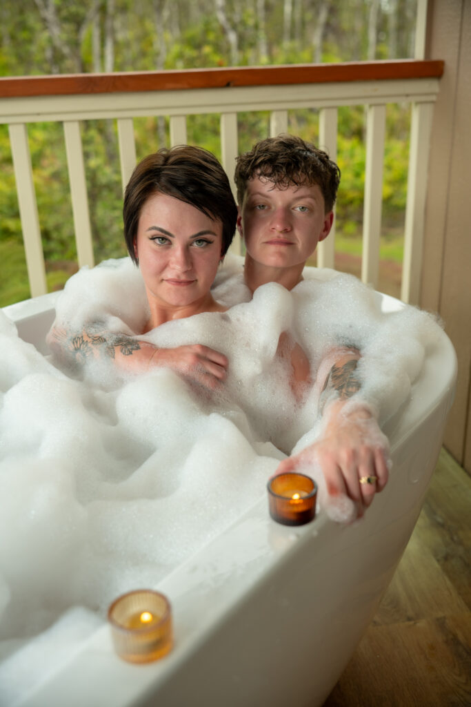 A couple sits in a bubble bath surrounded by candles on a lanai in Hawaii