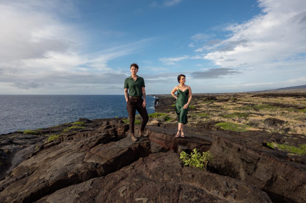 A couple stands on a lava rock formation with the Holei Sea Arch behind them