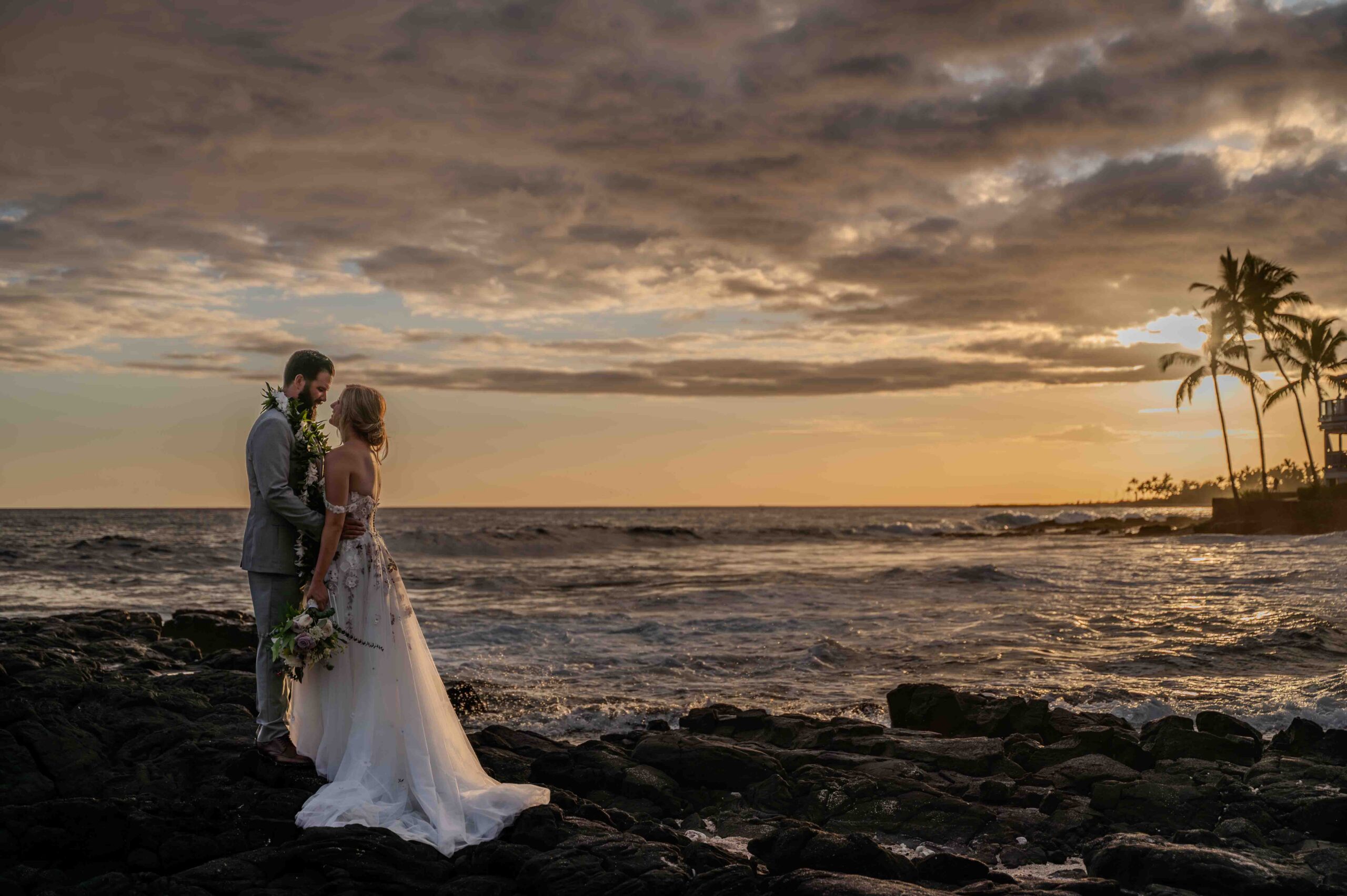 A couple stands on lava rocks at sunset after their Papa Kona Wedding