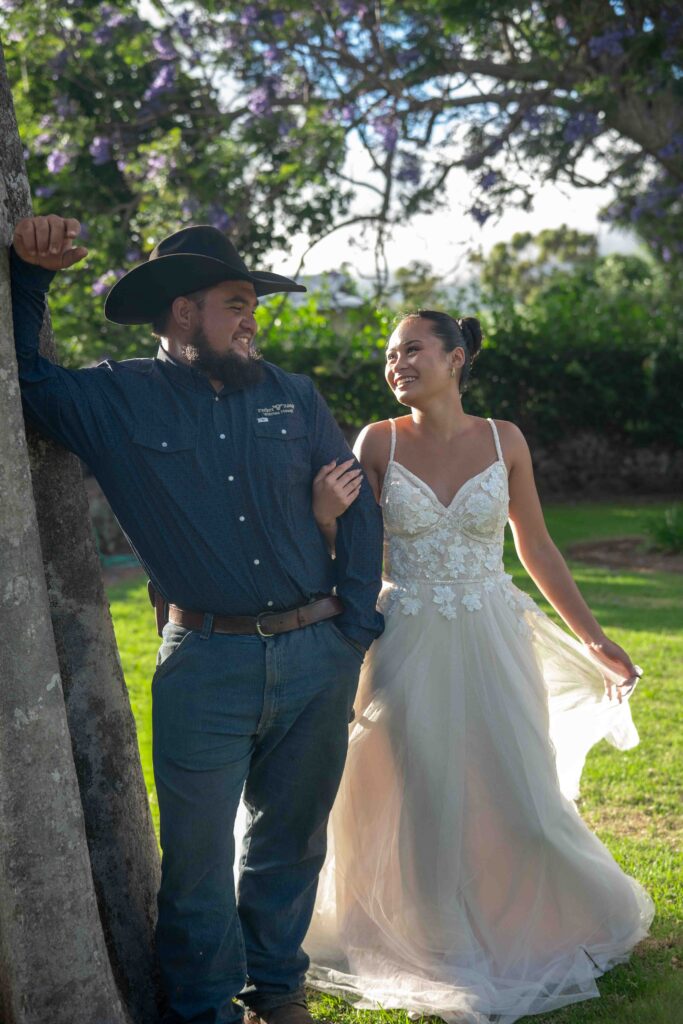A wedding couple stands together under a Jacaranda tree