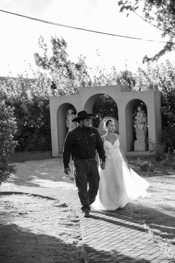 A bridal couple walks through the jacaranda square at Parker Ranch