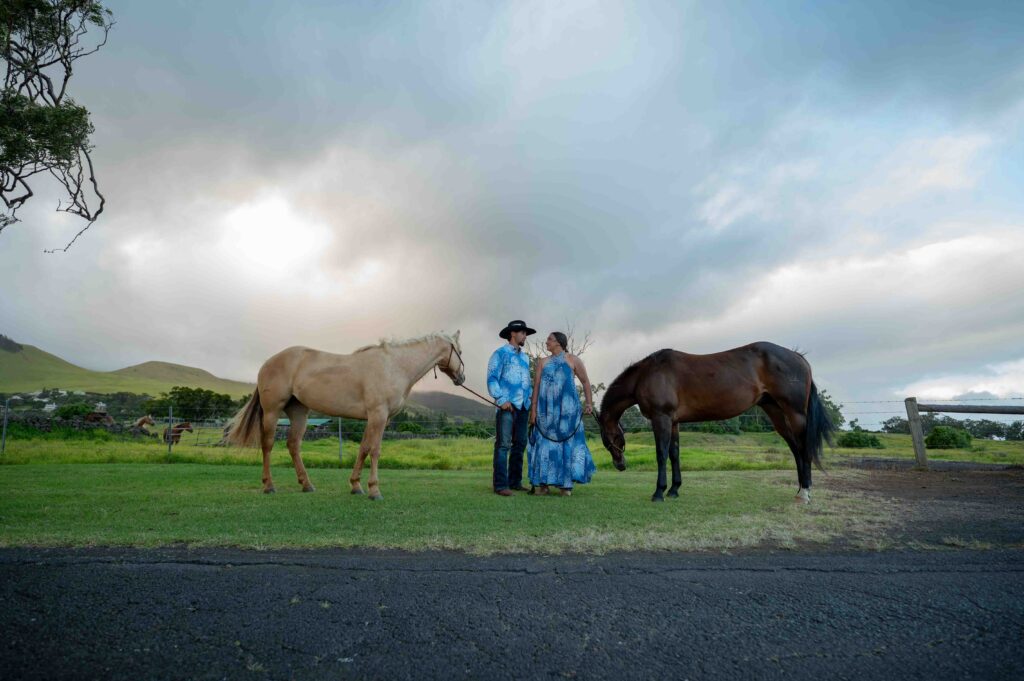 A couple stands between two horses on their wedding day