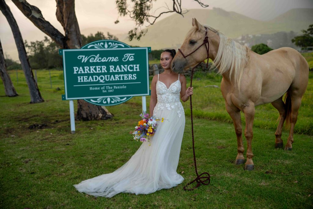 A bride and her horse stand near the Parker Ranch headquarters sign