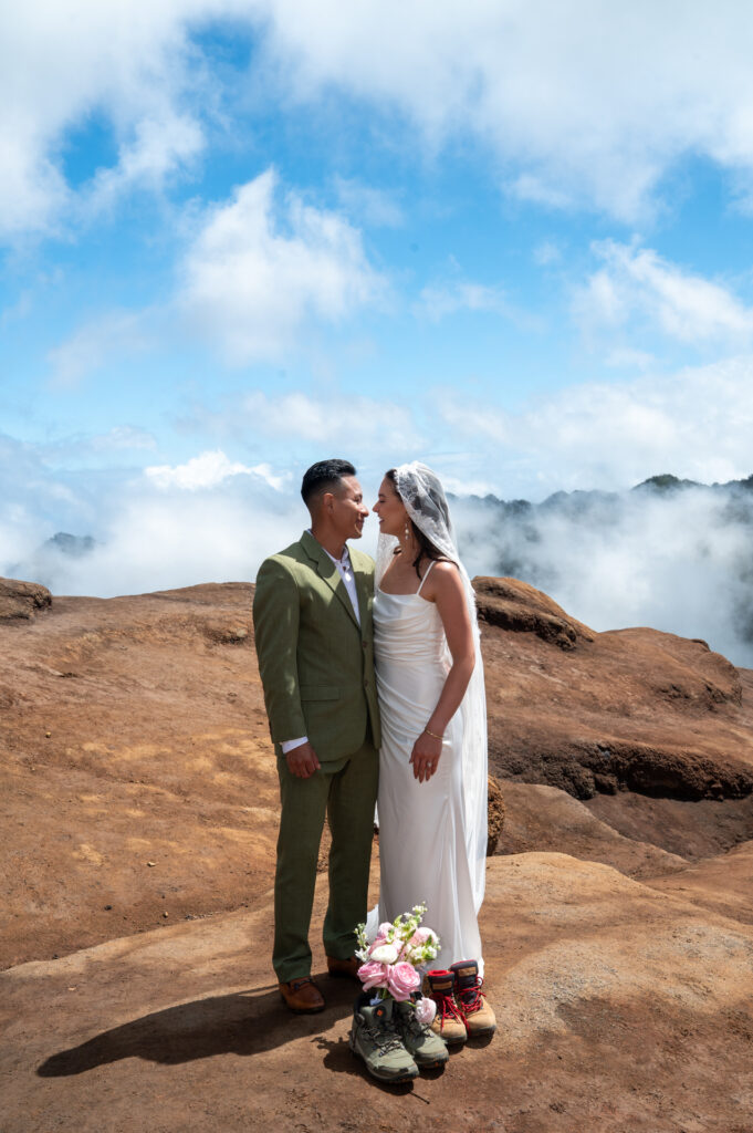 A couple poses with their hiking boots at Kalalau lookout after their Kauai elopement ceremony