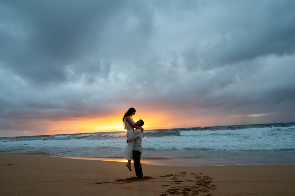 a groom lifts his bride up on the beach at sunrise for their Kauai elopement