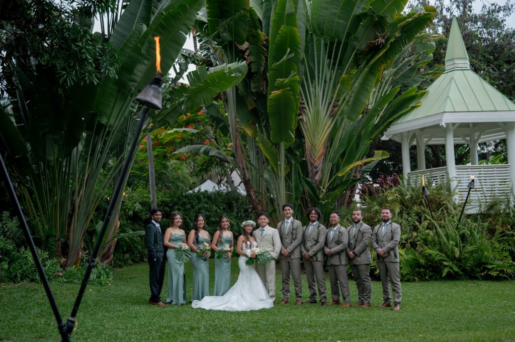 The entire wedding party poses for a photo under the gazebo of the Bayside Chapel lawn during an Outrigger Kona wedding