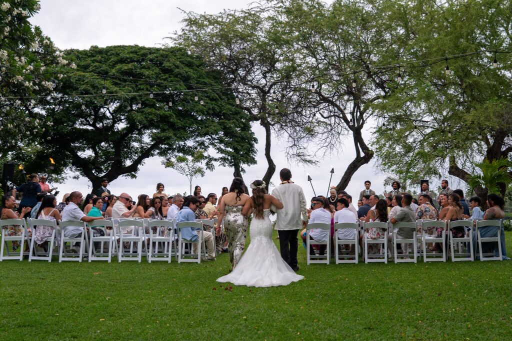 A bride is walked down the aisle of the Bayside Chapel Lawn at her Outrigger Kona wedding