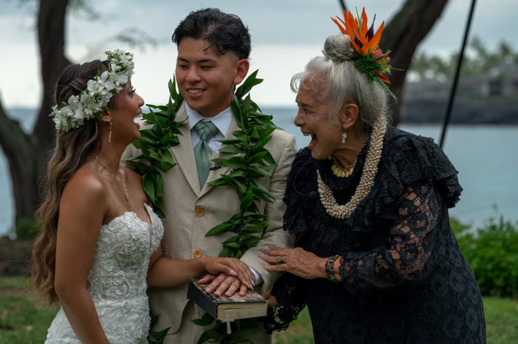 A bride and groom laugh with their wedding officiant during their Outrigger Kona wedding on the bayside chapel lawn