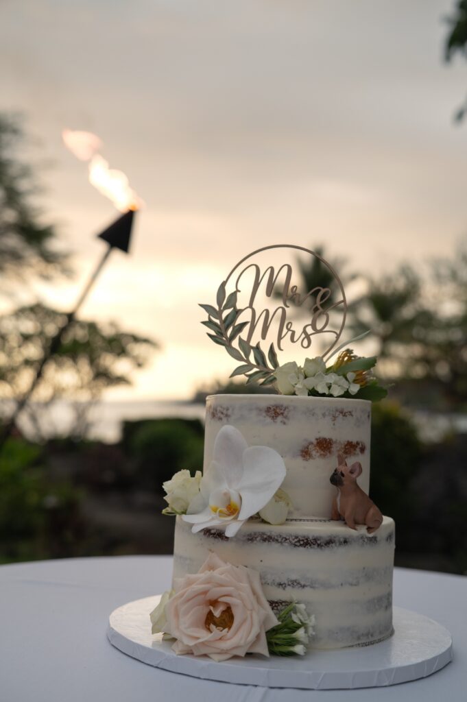 A wedding cake with a tiki torch and sunset in the background during an Outrigger Kona Wedding